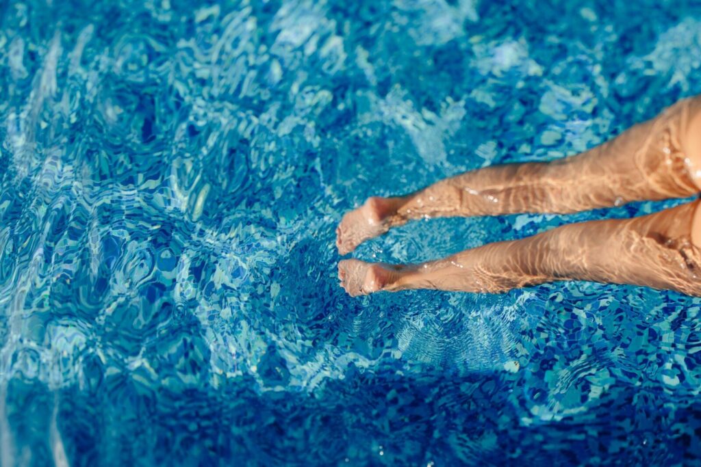 A person's legs submerged in clear blue water.